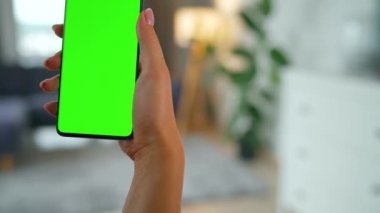 Evde dikey modda yeşil ekranlı akıllı telefon kullanan bir kadın var. Kız internette geziniyor, içeriği izliyor, videolar izliyor. POV.