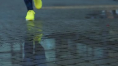 Bayan sporcu kadın dışarıda koşuyor, su birikintisine giriyor. Yağmurda koşan tek koşucu, su sıçratıyor. Yavaş çekim