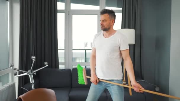 男人打扫房间，想象自己是个摇滚明星，像吉他一样弹奏扫帚. — 图库视频影像