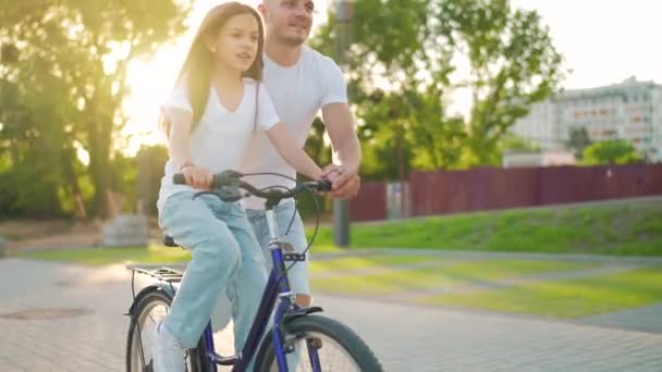 Tata uczy córkę jeździć na rowerze o zachodzie słońca. Zwolniony ruch — Wideo stockowe