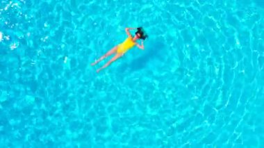 En tepeden, havuzda sırtüstü uzanmış sarı mayo giymiş bir kadın görüntüsü. Rahatlatıcı kavram