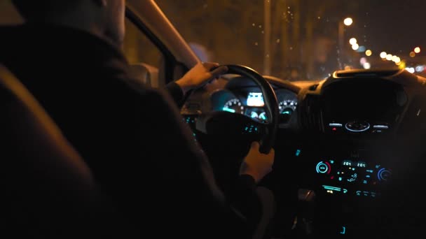 Muž projíždějící ulicemi nočního města. Pohled ze zadního sedadla auta. — Stock video