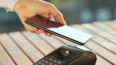 Akıllı telefondan yapılan temassız ödeme. Kablosuz ödeme konsepti. Yakın plan, kadın banka terminalindeki siparişi ödemek için akıllı telefon nakitsiz cüzdan teknolojisi kullanıyor..