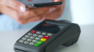 Akıllı telefondan yapılan temassız ödeme. Kablosuz ödeme konsepti. Yakın plan, kadın banka terminalindeki siparişi ödemek için akıllı telefon nakitsiz cüzdan teknolojisi kullanıyor..