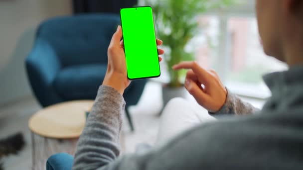 Mujer en casa usando smartphone con pantalla verde en modo vertical. Chica navegando por Internet, viendo contenido, videos — Vídeo de stock