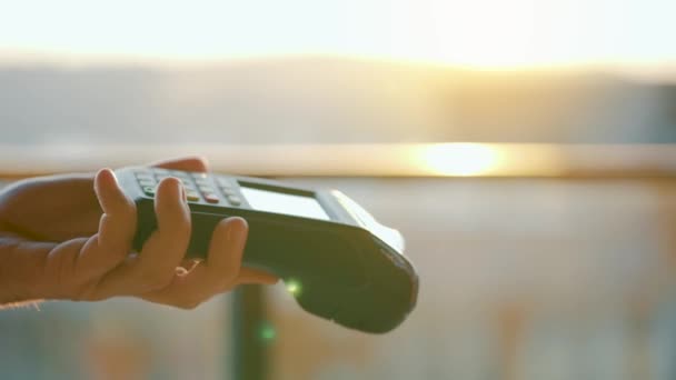 NFC pago con tarjeta de crédito. Mujer pagando con tarjeta de crédito sin contacto con tecnología NFC. Transacción inalámbrica de dinero. Máquina de tarjetas en mano masculina sobre fondo de luz solar — Vídeos de Stock