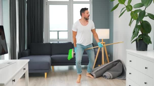 Hombre limpiando la casa y divirtiéndose bailando con una escoba. Movimiento lento — Vídeo de stock