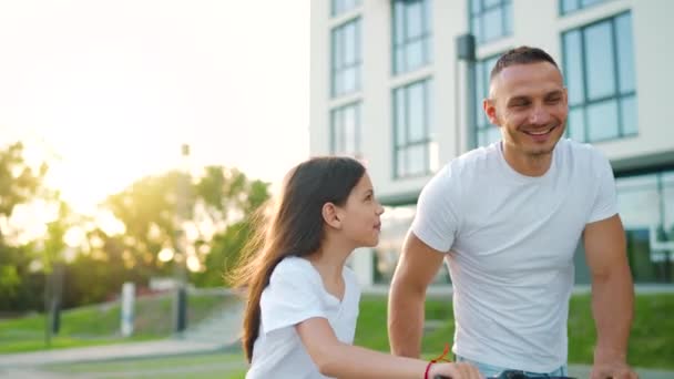 O pai está a ensinar a filha a andar de bicicleta ao pôr-do-sol. Movimento lento — Vídeo de Stock