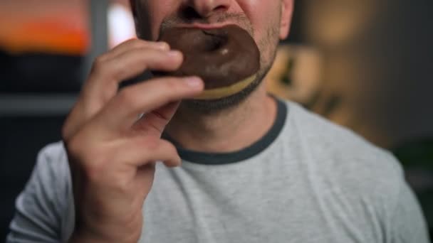 Чоловік поспішає їсти солодкий шоколадний пончик. Крупним планом — стокове відео