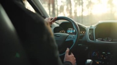 Adam yol boyunca araba sürüyor, batan güneş ön camda parlıyor.