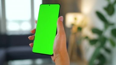 Evde dikey modda yeşil ekranlı akıllı telefon kullanan bir kadın var. Kız internette geziniyor, içeriği izliyor, videolar izliyor. POV.