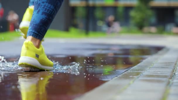 Female sports woman jogging outdoors, stepping into puddle. Single runner running in rain, making splash. Slow motion — Stock Video