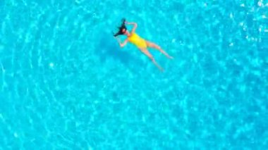 En tepeden, havuzda sırtüstü uzanmış sarı mayo giymiş bir kadın görüntüsü. Rahatlatıcı kavram