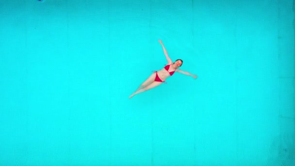Uitzicht vanaf de top als een vrouw in rood badpak liggend op haar rug in het zwembad. Ontspannend concept — Stockvideo
