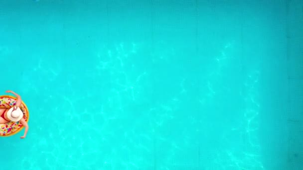 Havuzda donutun üzerinde yüzen kırmızı bikinili bir kadının hava görüntüsü. — Stok video