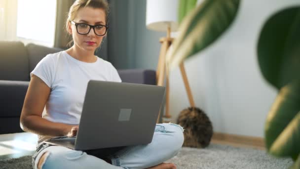 Gözlüklü kadın yerde oturuyor ve bir dizüstü bilgisayar üzerinde çalışıyor. Uzak çalışma kavramı. — Stok video