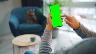 Evde dikey modda yeşil ekranlı akıllı telefon kullanan bir kadın var. Kız internette geziniyor, içeriği izliyor, videolar