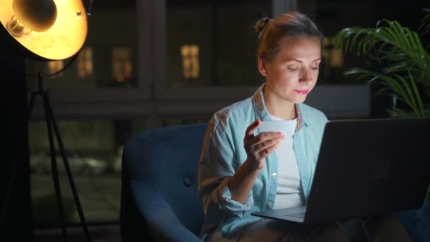한 여성 이 안락의자에 앉아 밤에 신용카드와 노트북을 사용하여 온라인 구매를 한다. — 비디오