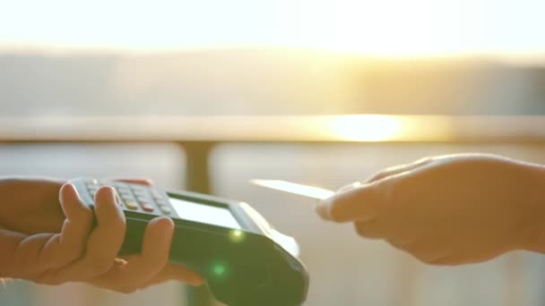 NFC 신용 카드 결제. NFC 기술로 비접 촉식 신용 카드를 지불하는 여성. 무궁무진 한 돈 거래. 햇빛을 배경으로 남자 손에 카드 기계를 쥐고 있는 모습 — 비디오