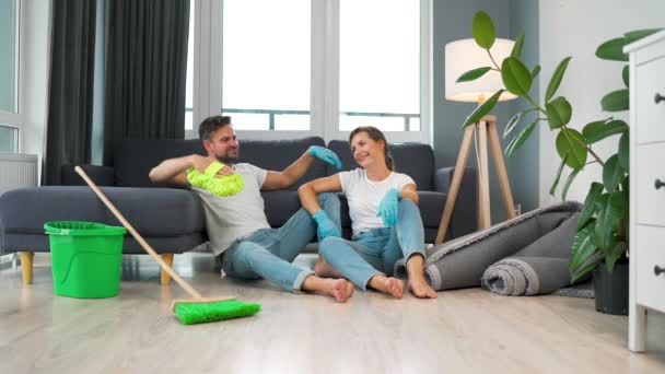 Casal cansado senta-se no chão em uma sala e alta cinco uns aos outros depois que eles terminam de limpar a casa. Movimento lento — Vídeo de Stock