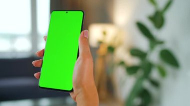 Evde dikey modda yeşil ekranlı akıllı telefon kullanan bir kadın var. Kız internette geziniyor, içeriği izliyor, videolar izliyor. POV.