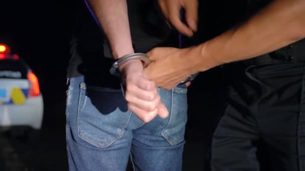 L'agente di polizia mette le manette all'uomo arrestato di notte e lo conduce a un'auto della polizia. — Video Stock