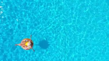 Havuzda donutun üzerinde yatan sarı mayo giymiş bir kadının hava manzarası.