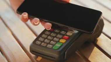 Akıllı telefondan yapılan temassız ödeme. Kablosuz ödeme konsepti. Yakın plan, kadın banka terminalindeki siparişi ödemek için akıllı telefon nakitsiz cüzdan teknolojisi kullanıyor..