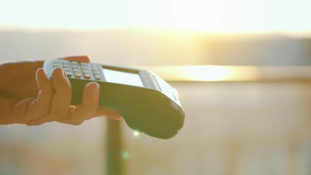 Close-up, wanita yang menggunakan teknologi smartphone cashless wallet NFC untuk membayar pesanan di terminal bank. Mesin kartu di tangan pria di latar belakang sinar matahari — Stok Video