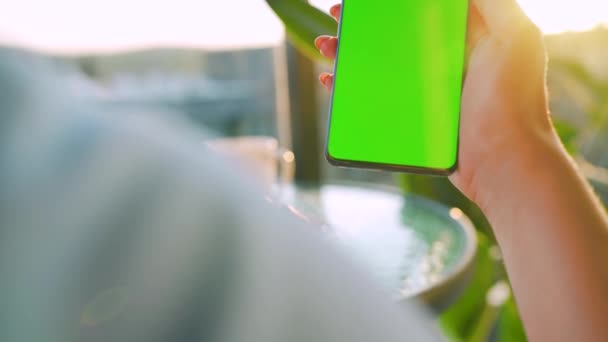 Mujer sentada en un café y usando smartphone con pantalla verde en modo vertical. Chica navegando por Internet, viendo contenido, videos, blogs. — Vídeos de Stock