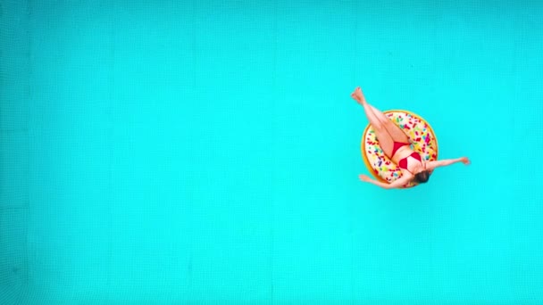 Luchtfoto van een vrouw in rode bikini zwemmend op een donut in het zwembad — Stockvideo