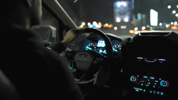 Un hombre conduciendo por las calles de la ciudad nocturna. Vista desde el asiento trasero del coche. — Vídeos de Stock