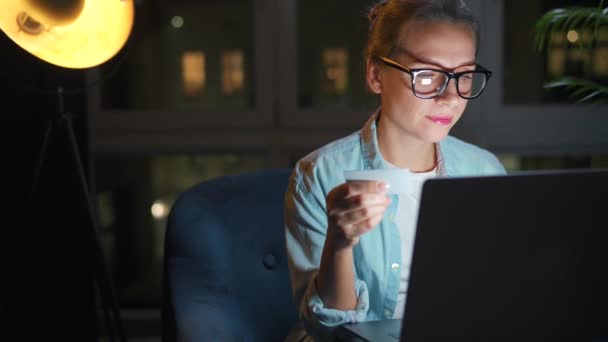 Mujer está sentado en el sillón y hace una compra en línea con una tarjeta de crédito y un ordenador portátil por la noche. — Vídeo de stock