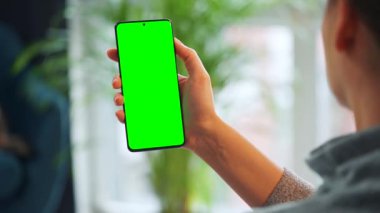Evde dikey modda yeşil ekranlı akıllı telefon kullanan bir kadın var. Kız internette geziniyor, içeriği izliyor, videolar