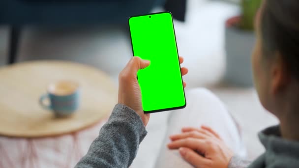 Женщина дома использует смартфон с зеленым макетом экрана в вертикальном режиме. Девочки просматривают Интернет, смотрят контент, видео — стоковое видео