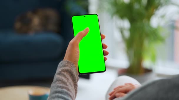 Mujer en casa usando smartphone con pantalla verde en modo vertical. Chica navegando por Internet, viendo contenido, videos — Vídeos de Stock