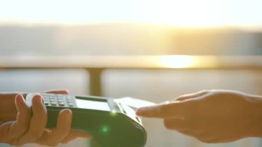NFC kredi kartı ödemesi. NFC teknolojisiyle kredi kartıyla ödeme yapan bir kadın. Kablosuz para transferi. Kart makinesi erkek eliyle güneş ışığı arkaplanında