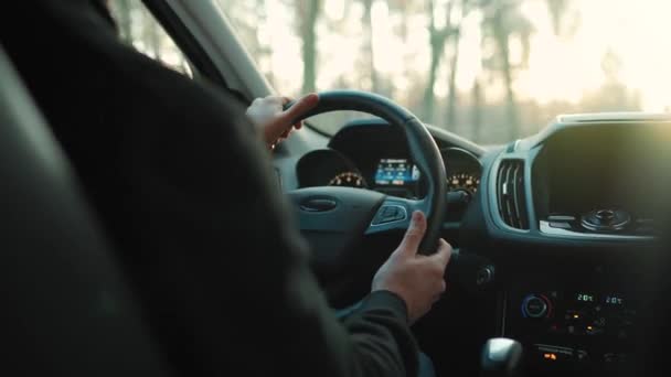 De mens rijdt een auto langs de weg, de ondergaande zon schijnt in de voorruit — Stockvideo