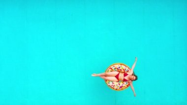 Havuzda donutun üzerinde yüzen kırmızı bikinili bir kadının hava görüntüsü.