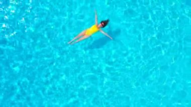 En tepeden, havuzda sırtüstü uzanmış sarı mayo giymiş bir kadın görüntüsü. Rahatlatıcı kavram