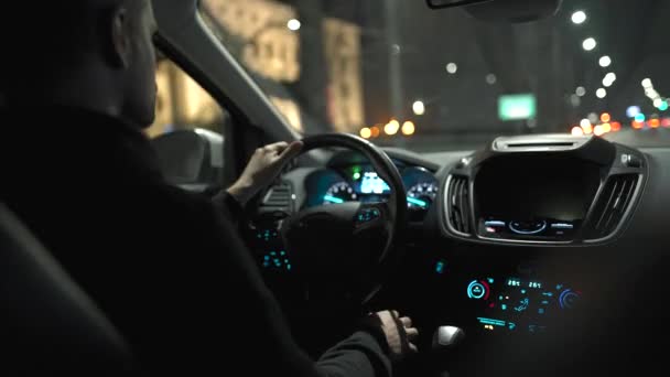 Gece şehrinin sokaklarında araba süren bir adam. Arabanın arka koltuğundan bak.. — Stok video