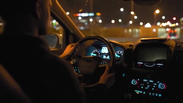 Un hombre conduciendo por las calles de la ciudad nocturna. Vista desde el asiento trasero del coche. — Vídeos de Stock