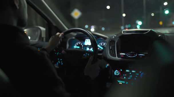 Un hombre conduciendo por las calles de la ciudad nocturna. Vista desde el asiento trasero del coche. — Vídeos de Stock