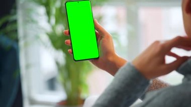 Evde dikey modda yeşil ekranlı akıllı telefon kullanan bir kadın var. Kız internette geziniyor, içeriği izliyor, videolar