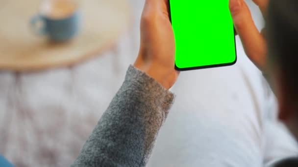 Kobieta w domu za pomocą smartfona z zielonym ekranem makiety w trybie pionowym. Dziewczyna przeglądająca Internet, oglądająca treści, filmy — Wideo stockowe