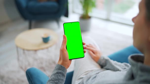 Mujer en casa usando smartphone con pantalla verde en modo vertical. Chica navegando por Internet, viendo contenido, videos — Vídeo de stock