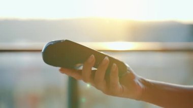 Yakın plan, adam banka terminalindeki siparişi ödemek için akıllı telefon nakitsiz cüzdan teknolojisi kullanıyor. Kart makinesi erkek eliyle güneş ışığı arkaplanında