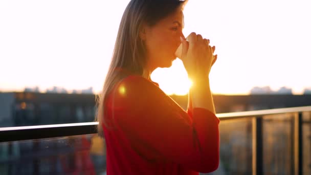 Donna in abito rosso con una tazza di caffè in piedi sul balcone e ammirare il tramonto. Rallentatore — Video Stock