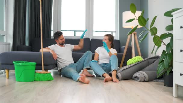 Pasangan lelah duduk di lantai di sebuah ruangan dan saling tos setelah mereka selesai membersihkan rumah — Stok Video
