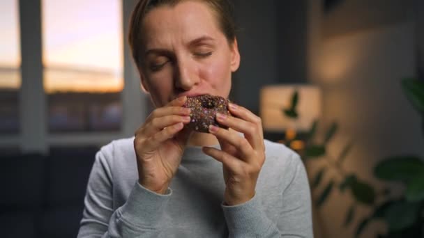 Dulce concepto de adicción. Una mujer come un donut de chocolate con deleite mórbido. — Vídeo de stock